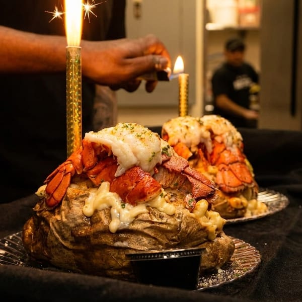 Chef lighting sparklers on two baked potatoes topped with lobster and mac and cheese.